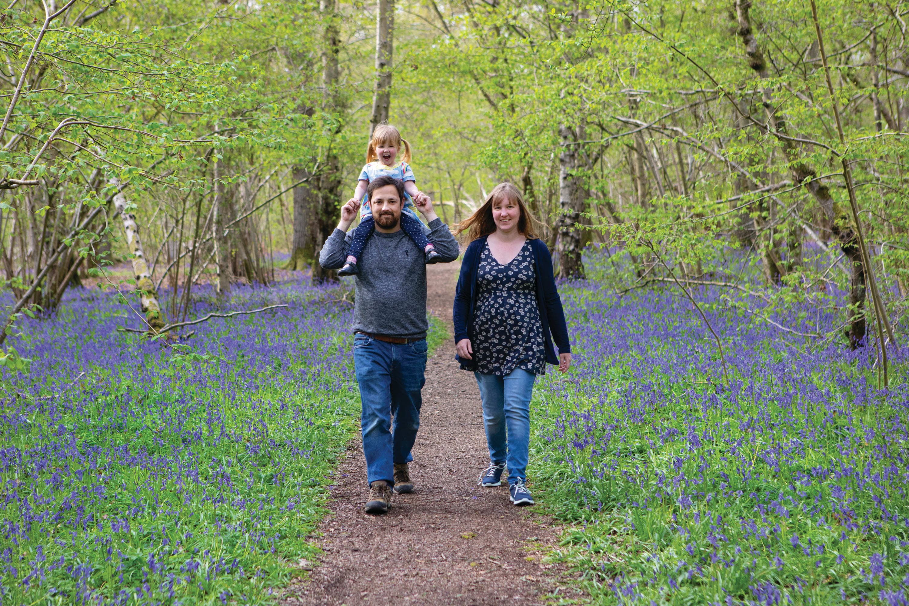 A man and woman walking through a forest with a child on their shoulders