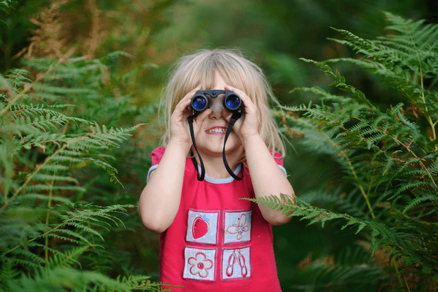 A little girl looking through binoculars in a forest