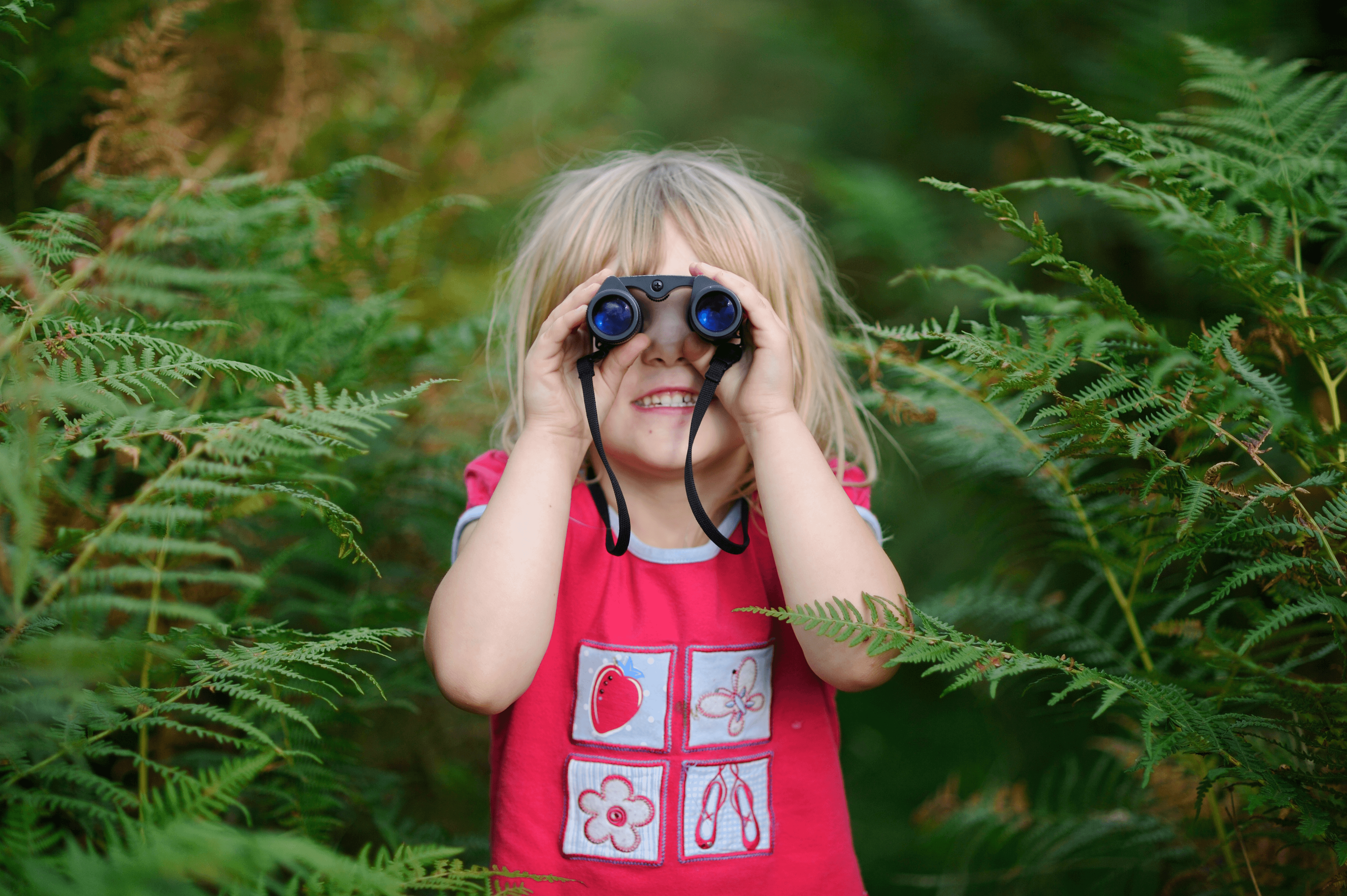 A little girl looking through binoculars in a forest