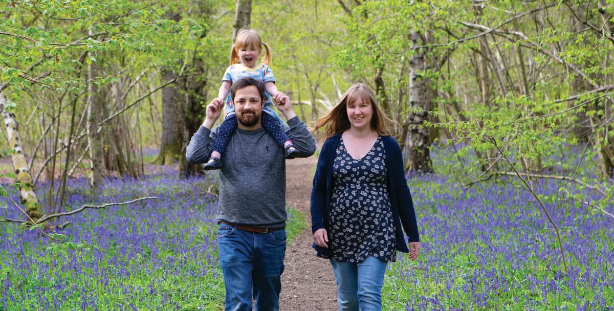 A man and woman walking through a forest with a child on their shoulders