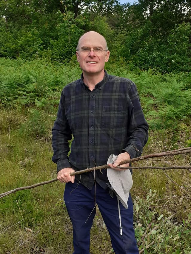 A man standing in a field holding a broken tree branch